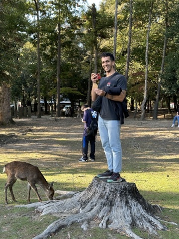 Francisco standing on a tree stump in Nara, Japan, with a deer nearby